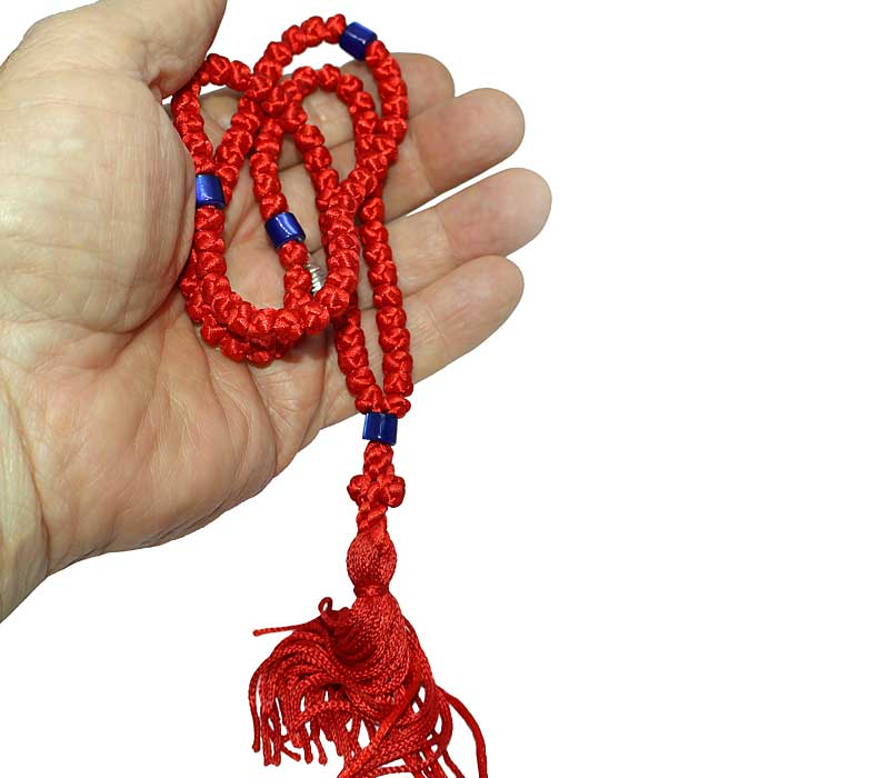 Red prayer rope with blue beads held in a hand against a white background