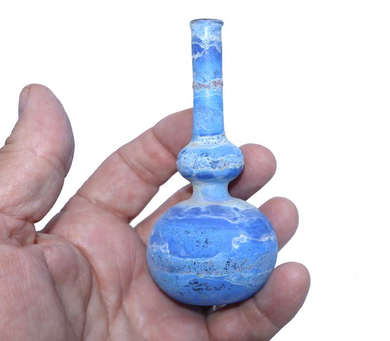 Hand holding a blue glass bottle with a white marbled pattern on a white background